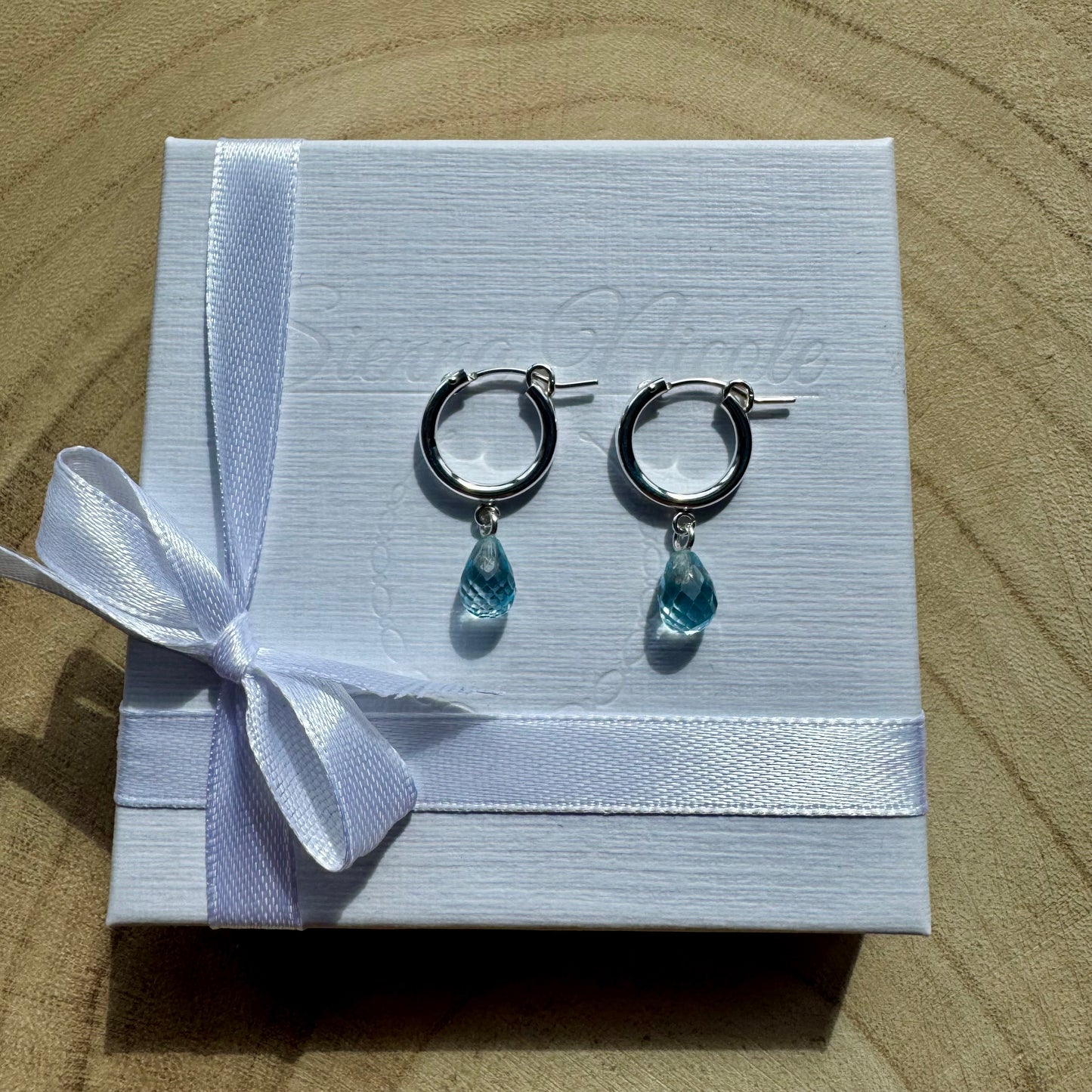 Sterling silver hoop earrings with teardrop-shaped blue topaz charms on gift packaging