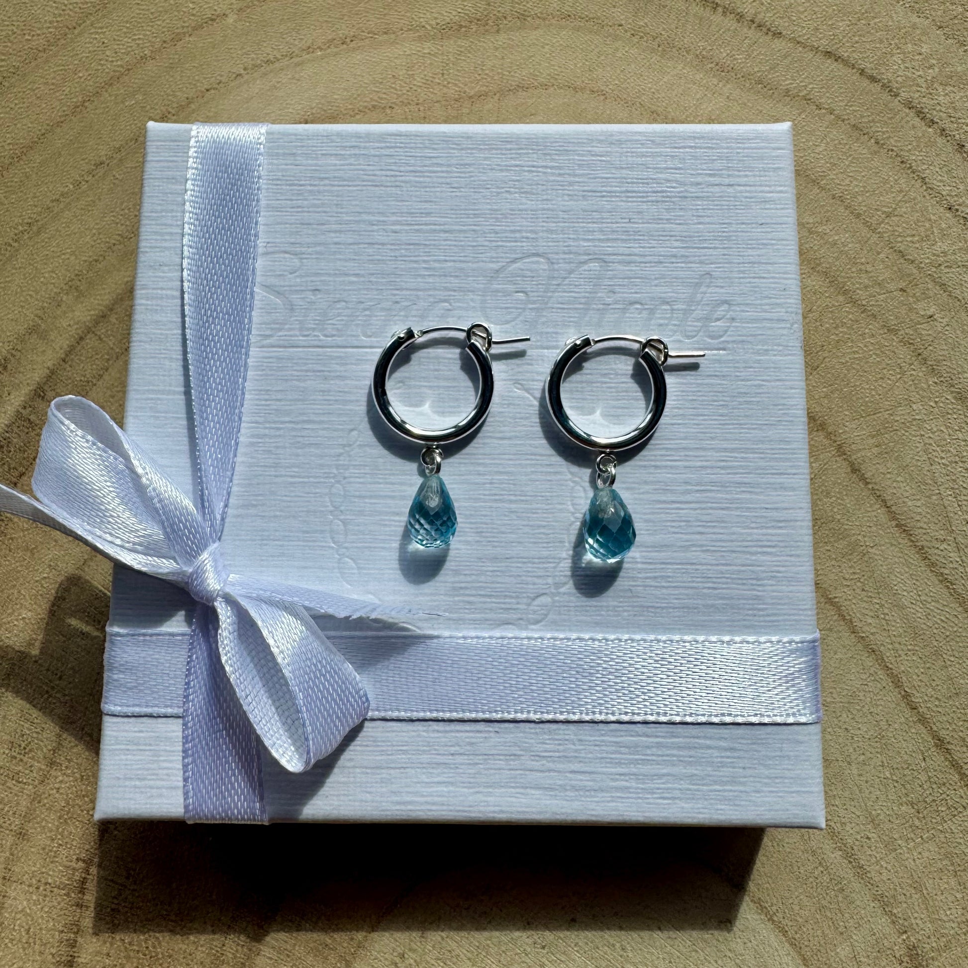 Sterling silver hoop earrings with teardrop-shaped blue topaz charms on gift packaging
