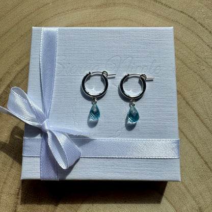 Sterling silver hoop earrings with teardrop-shaped blue topaz charms on gift packaging