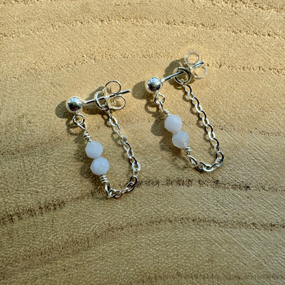 Pair of sterling silver chain earrings with blue chalcedony beads on a wooden surface
