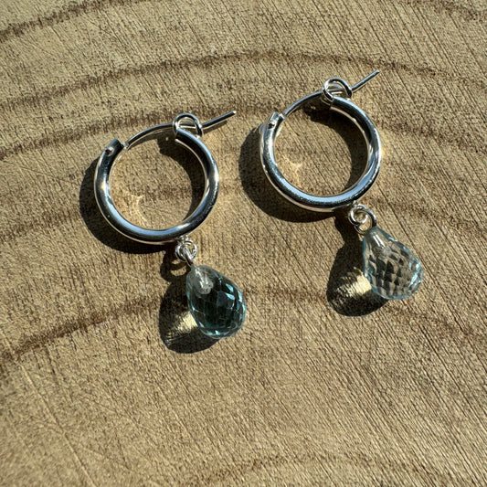 Sterling silver hoop earrings with teardrop-shaped blue topaz charms on a wooden surface