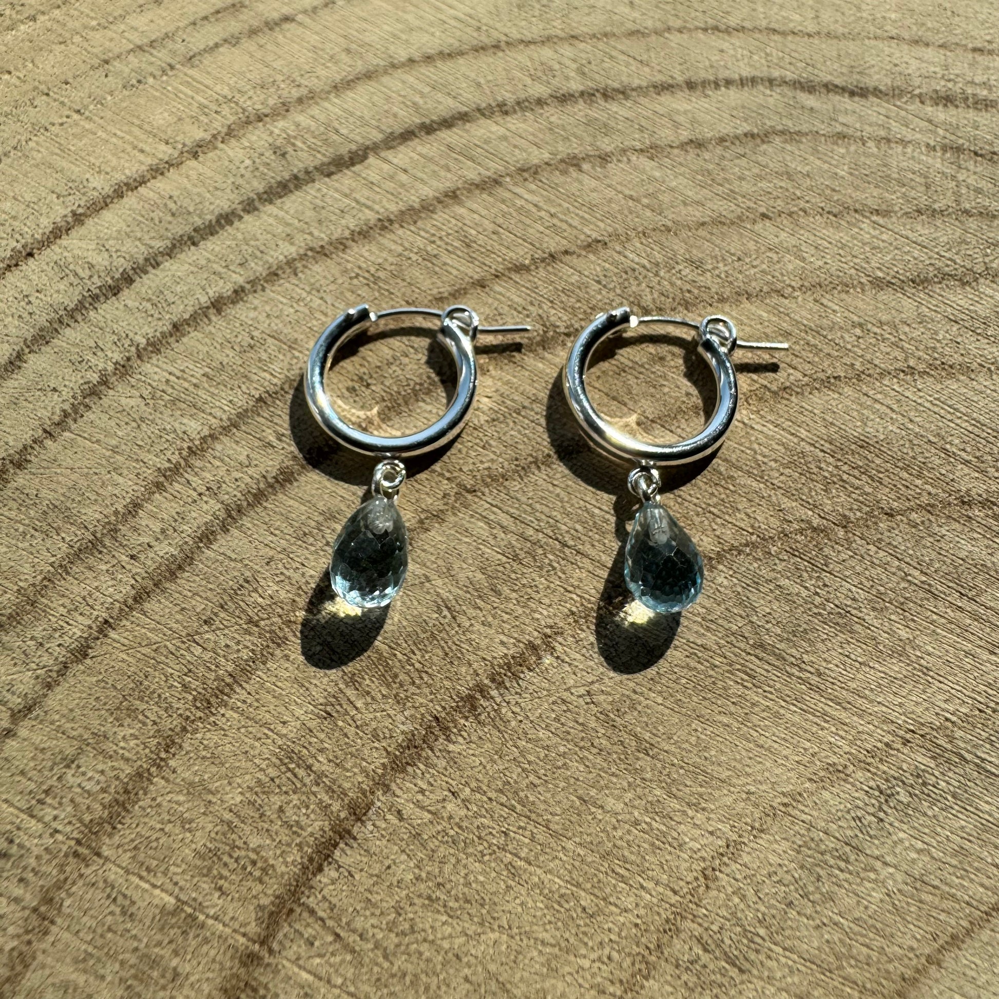 Sterling silver hoop earrings with teardrop-shaped blue topaz charms on a wooden surface