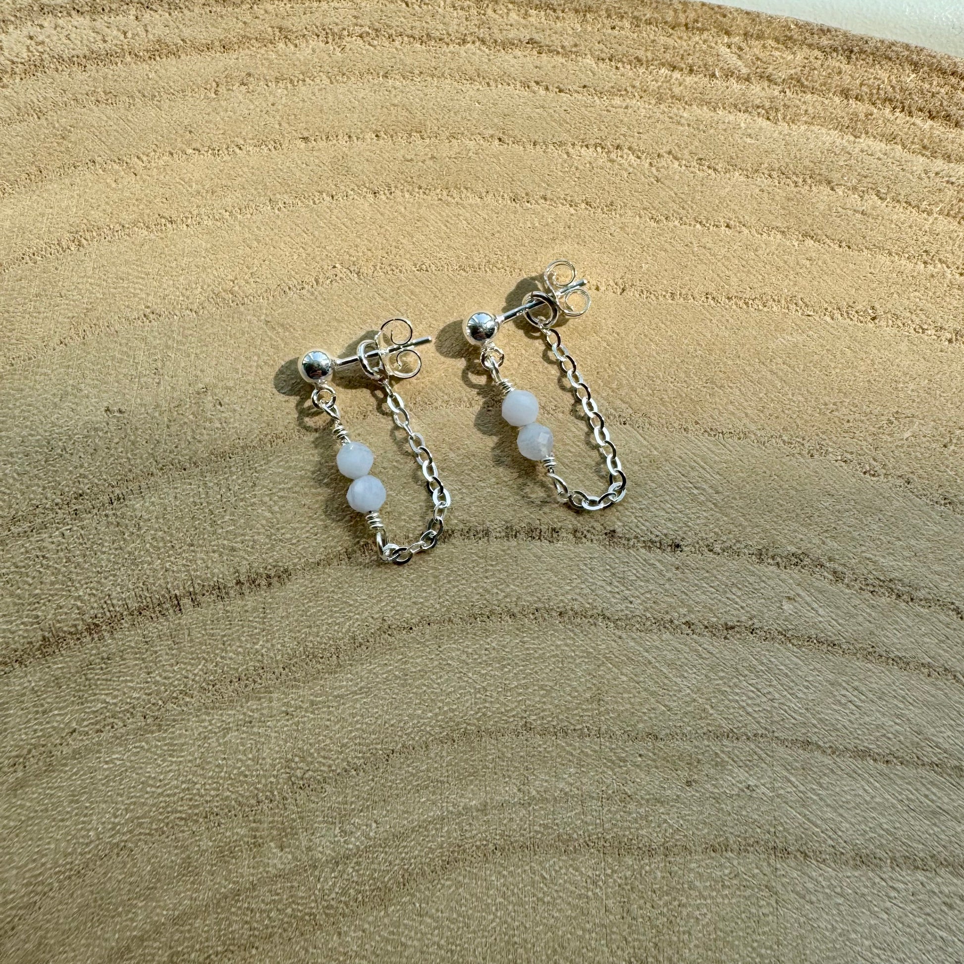 Pair of sterling silver chain earrings with blue chalcedony beads on a wooden surface zoomed out