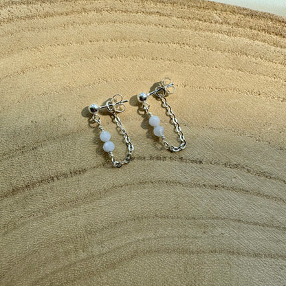 Pair of sterling silver chain earrings with blue chalcedony beads on a wooden surface zoomed out