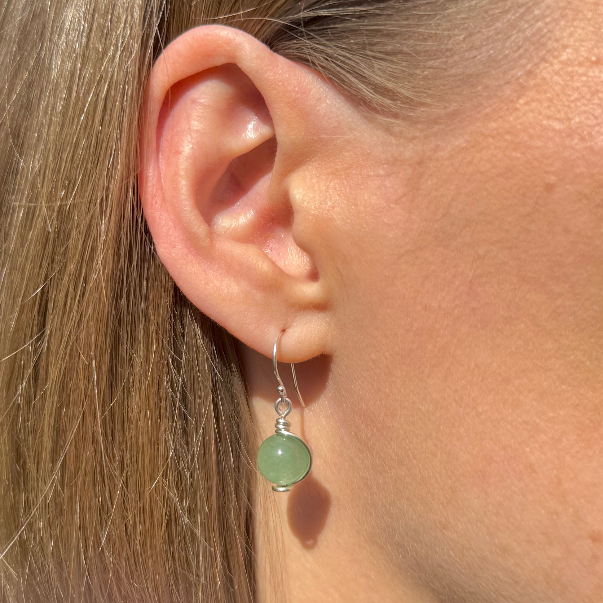 Close-up of an ear wearing a Sterling silver and green aventurine gemstone drop earring with a blurred background