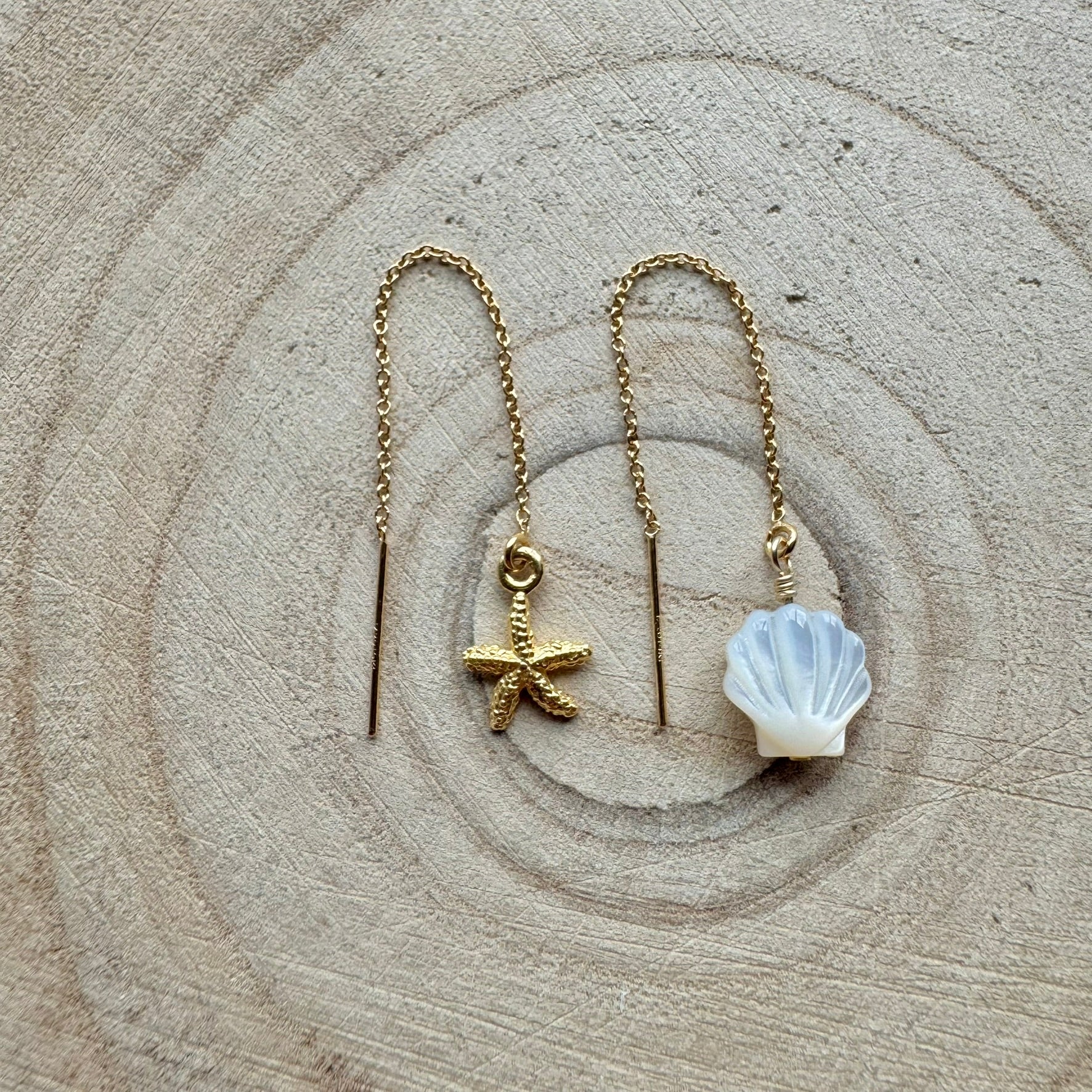 Gold threader earrings with starfish and shell charms on a wooden background