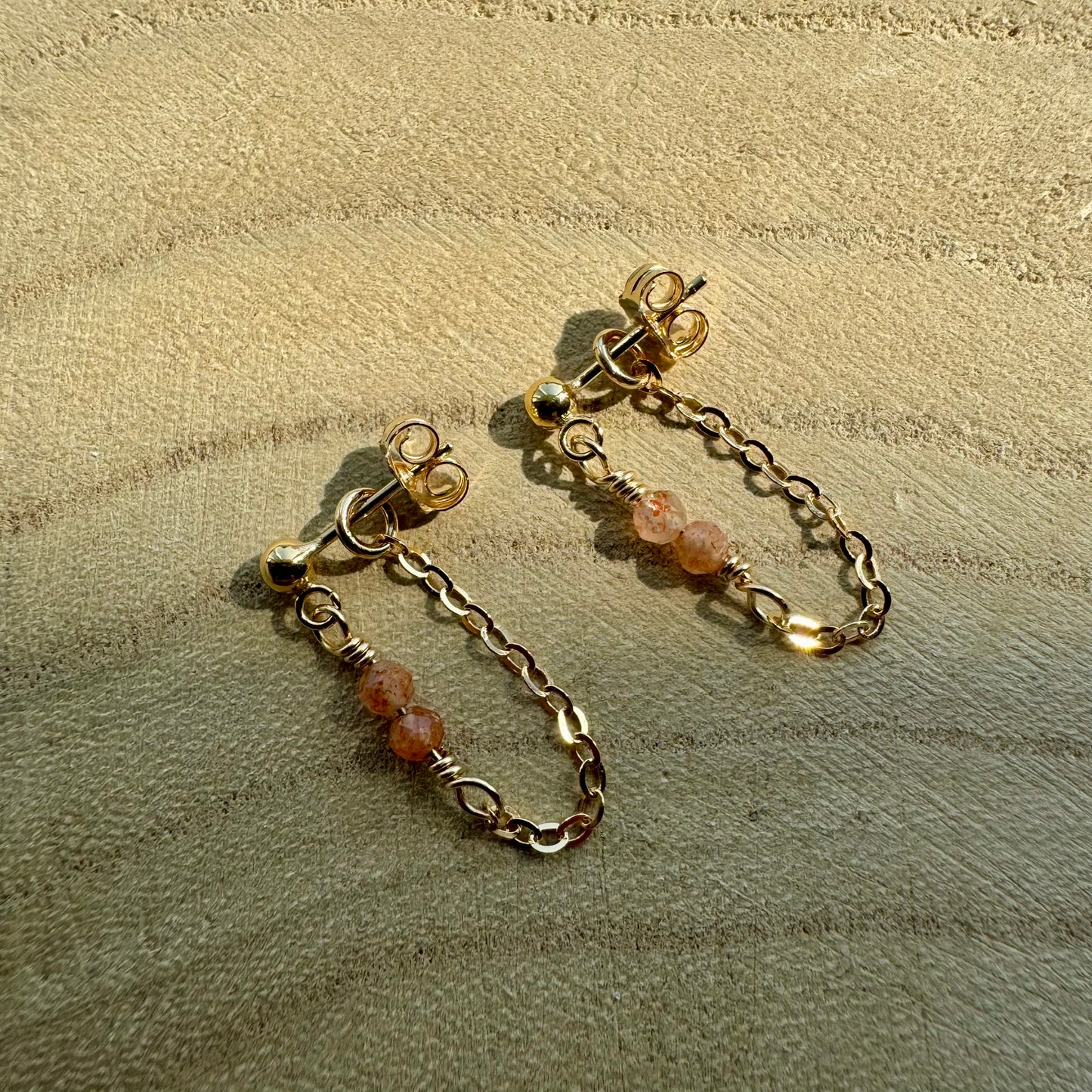 Gold filled chain and gemstone drop earrings on wooden surface