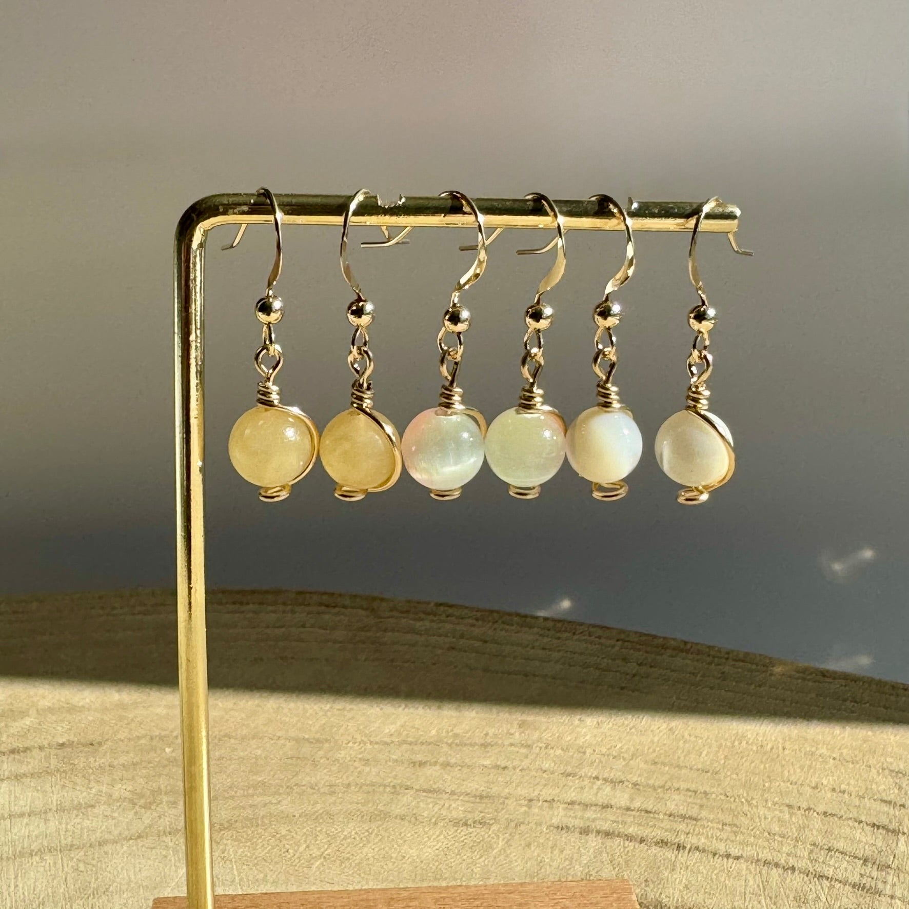 Set of gold filled wire-wrapped gemstone earrings on a gold stand against a neutral background