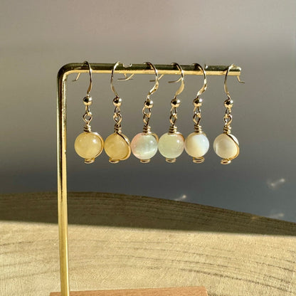 Set of gold filled wire-wrapped gemstone earrings on a gold stand against a neutral background