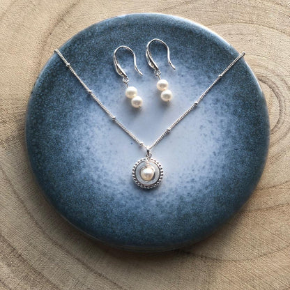 Pearl necklace and earrings on a blue stone surface