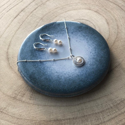 Silver jewelry set including earrings and a necklace on a blue stone surface.