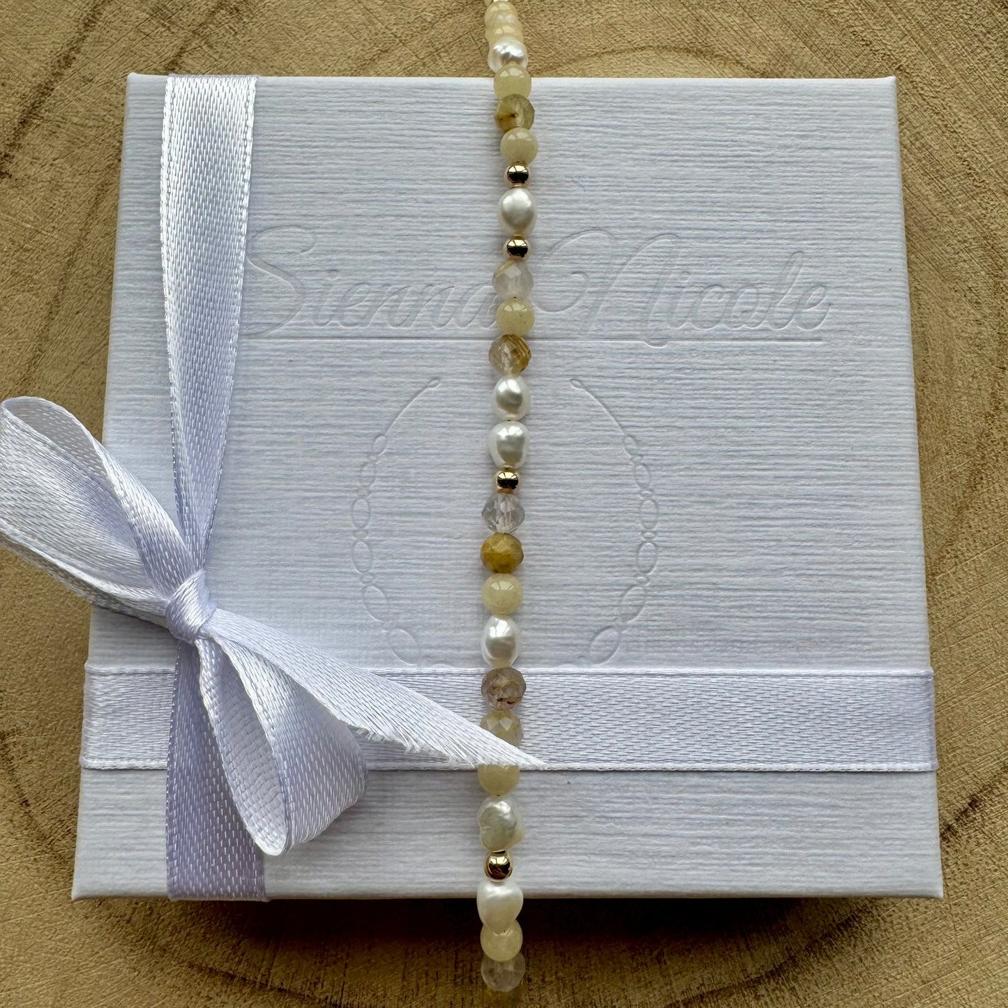 Vertical view of pearl and mixed gemstone bracelet with gold filled details on gift packaging