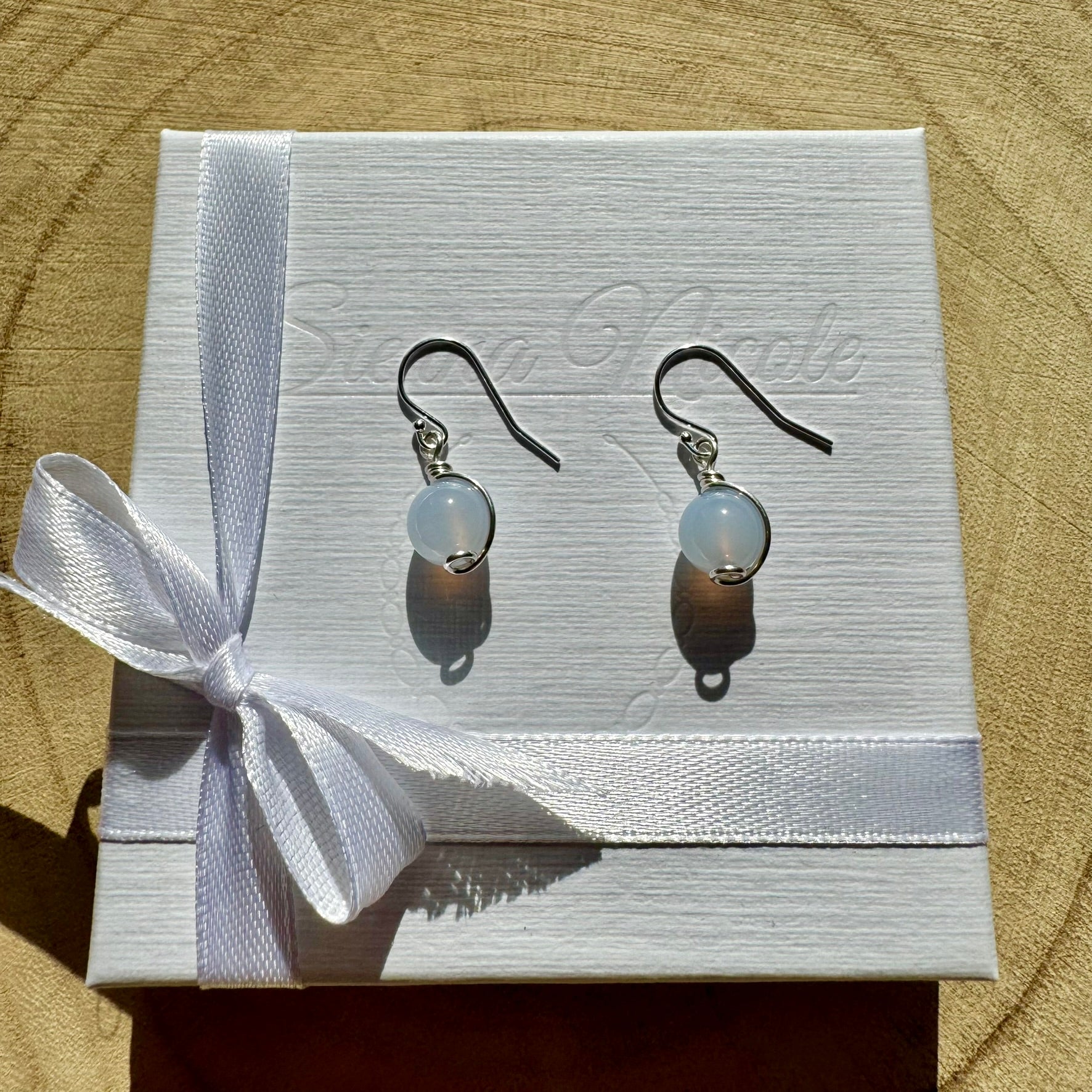 Pair of sterling silver gemstone drop earrings on a white box with a ribbon, against a wooden background