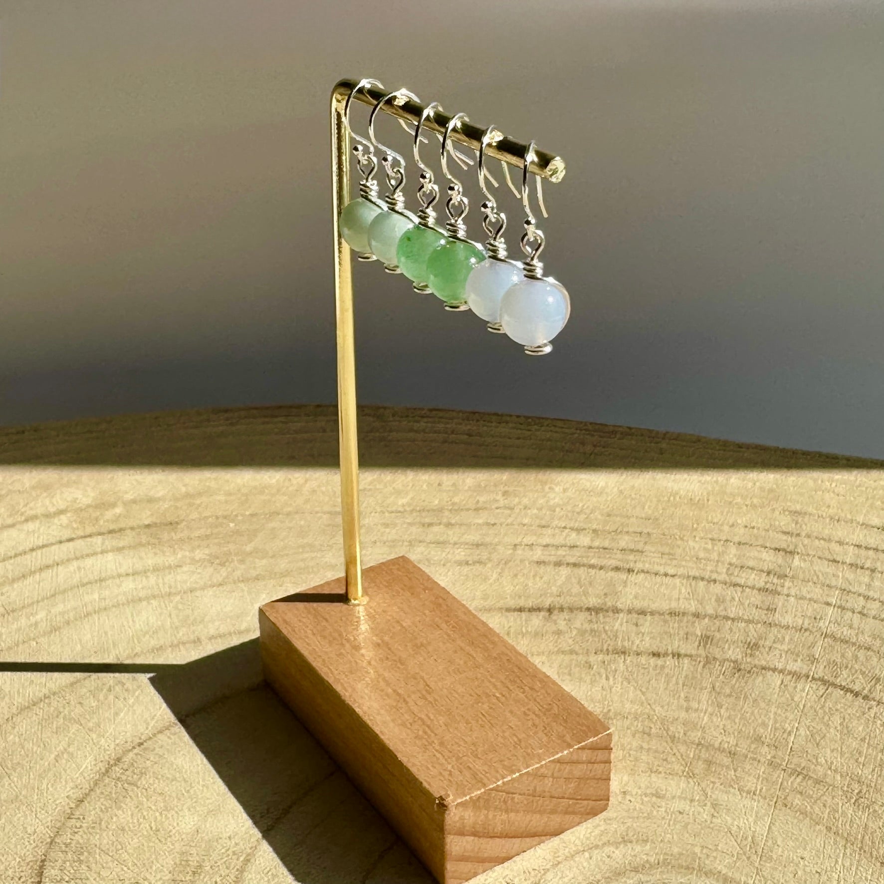 Set of sterling silver drop earrings with green aventurine, blue aquamarine and blue chalcedony gemstones on a wooden stand against a neutral background
