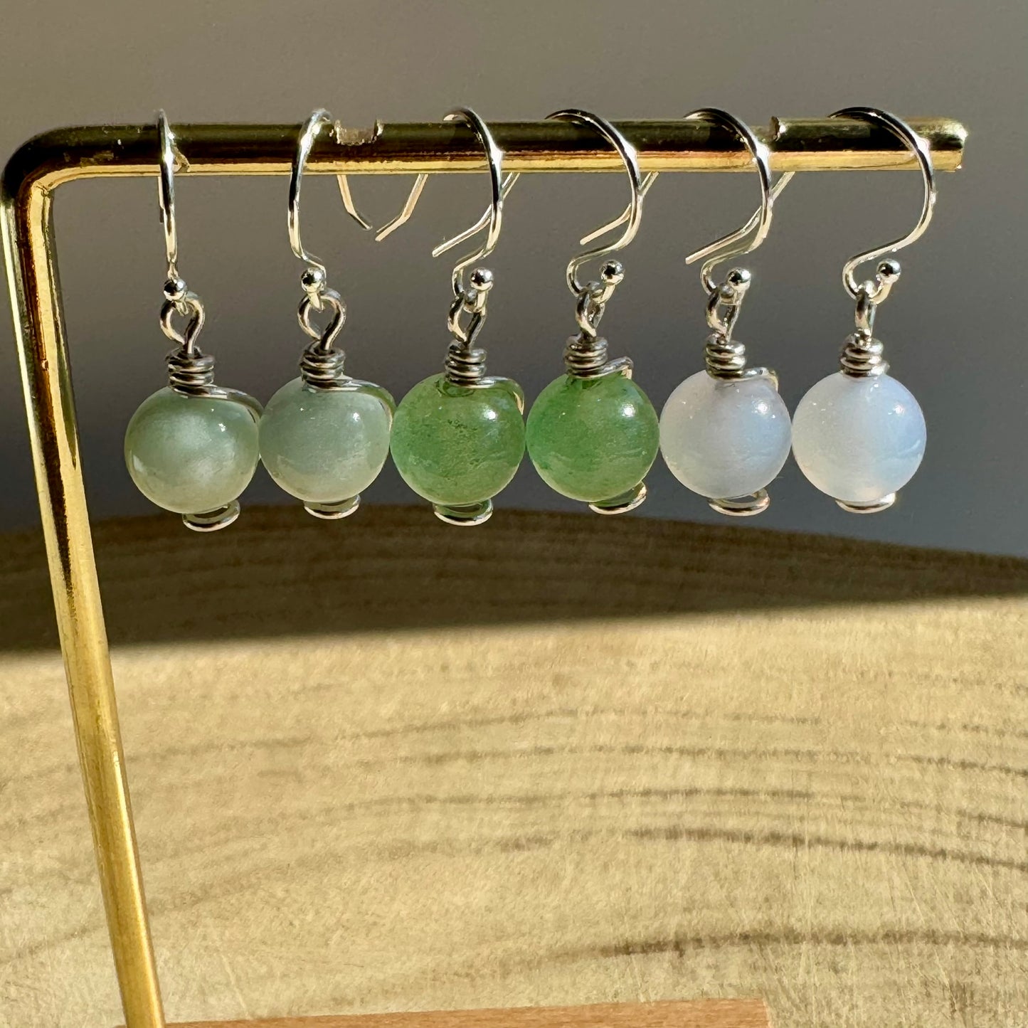 Set of Sterling Silver drop earrings with green aventurine, blue aquamarine and blue chalcedony gemstones on a gold stand.