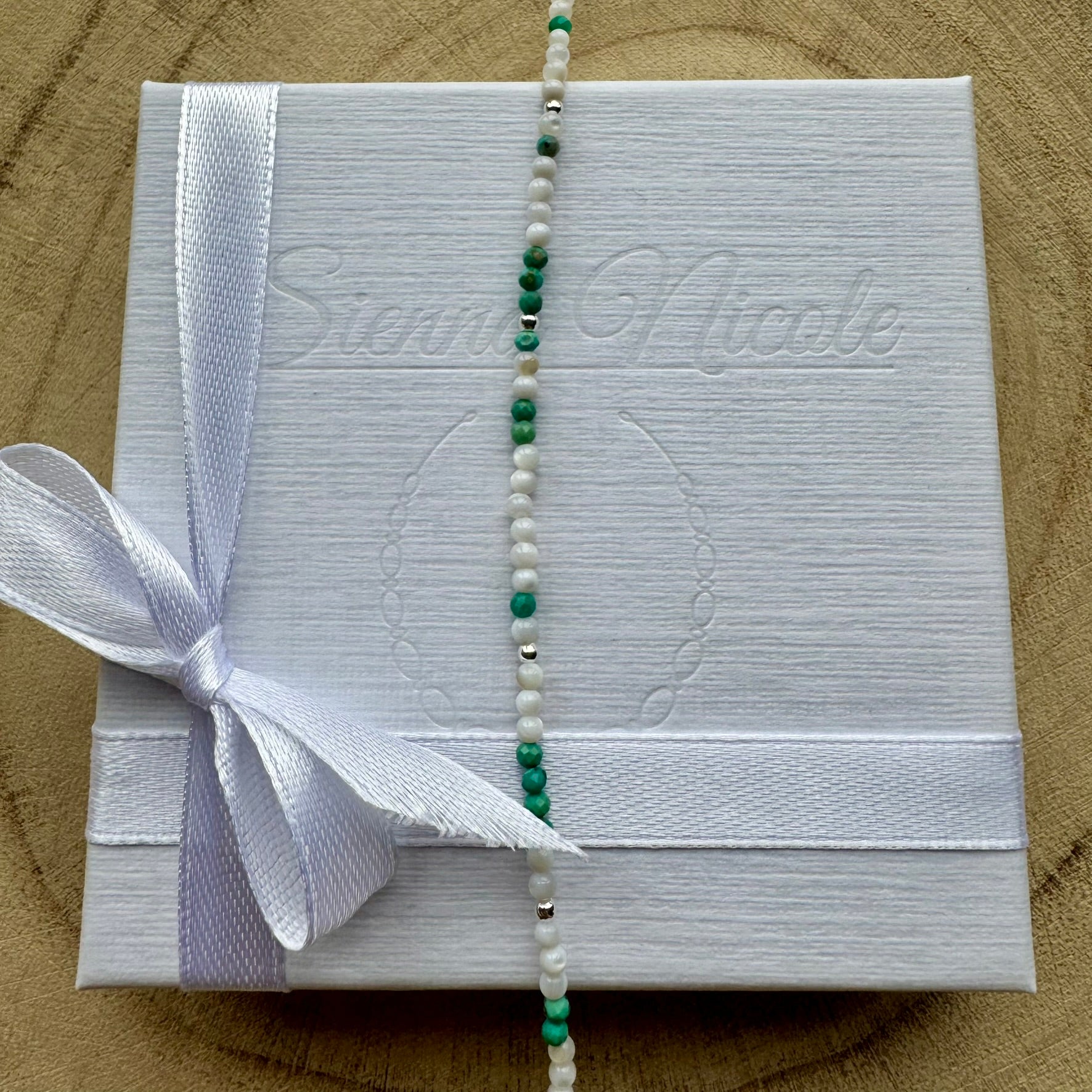 Vertical view of a mother of pearl and turquoise bracelet on gift packaging