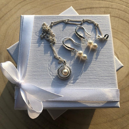 Silver necklace and earrings on a white box with a white ribbon, set against a wooden surface.