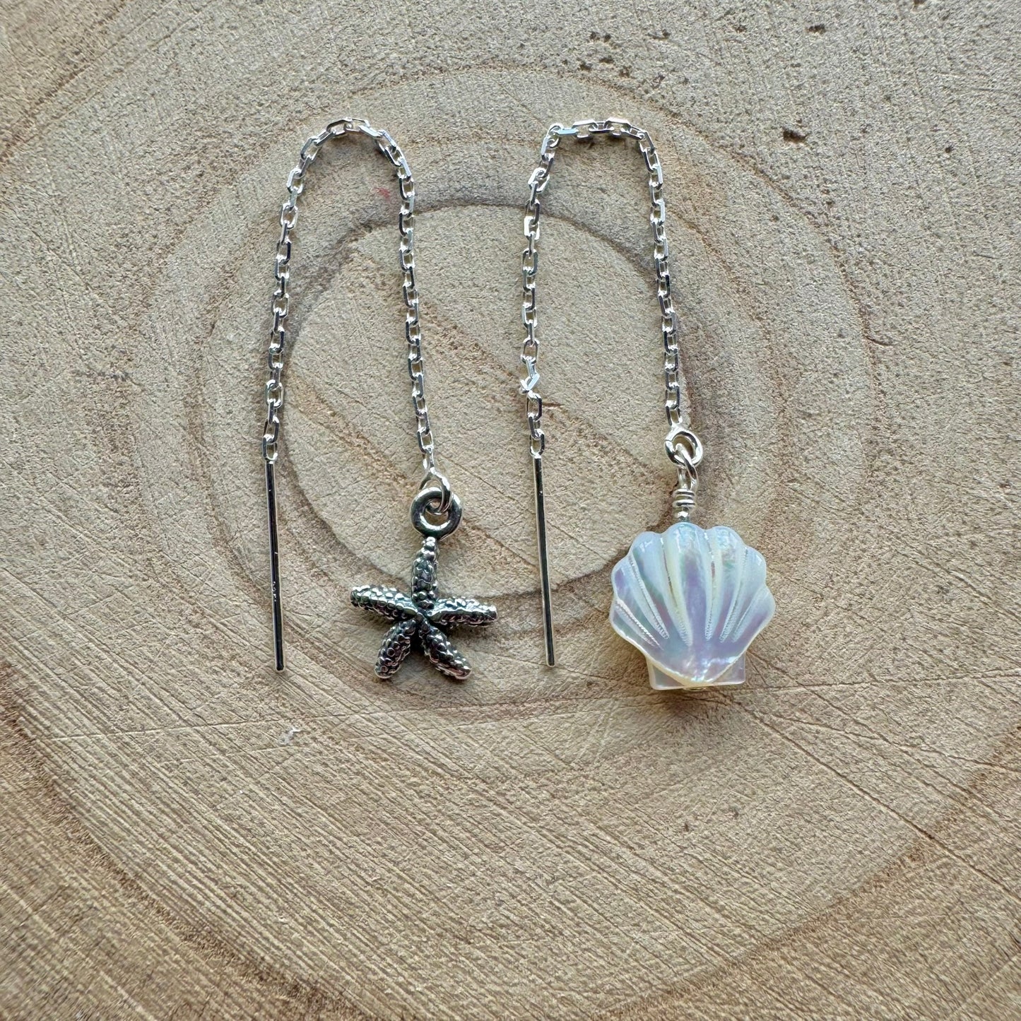 Silver threader earrings with starfish and shell charms on a wooden background