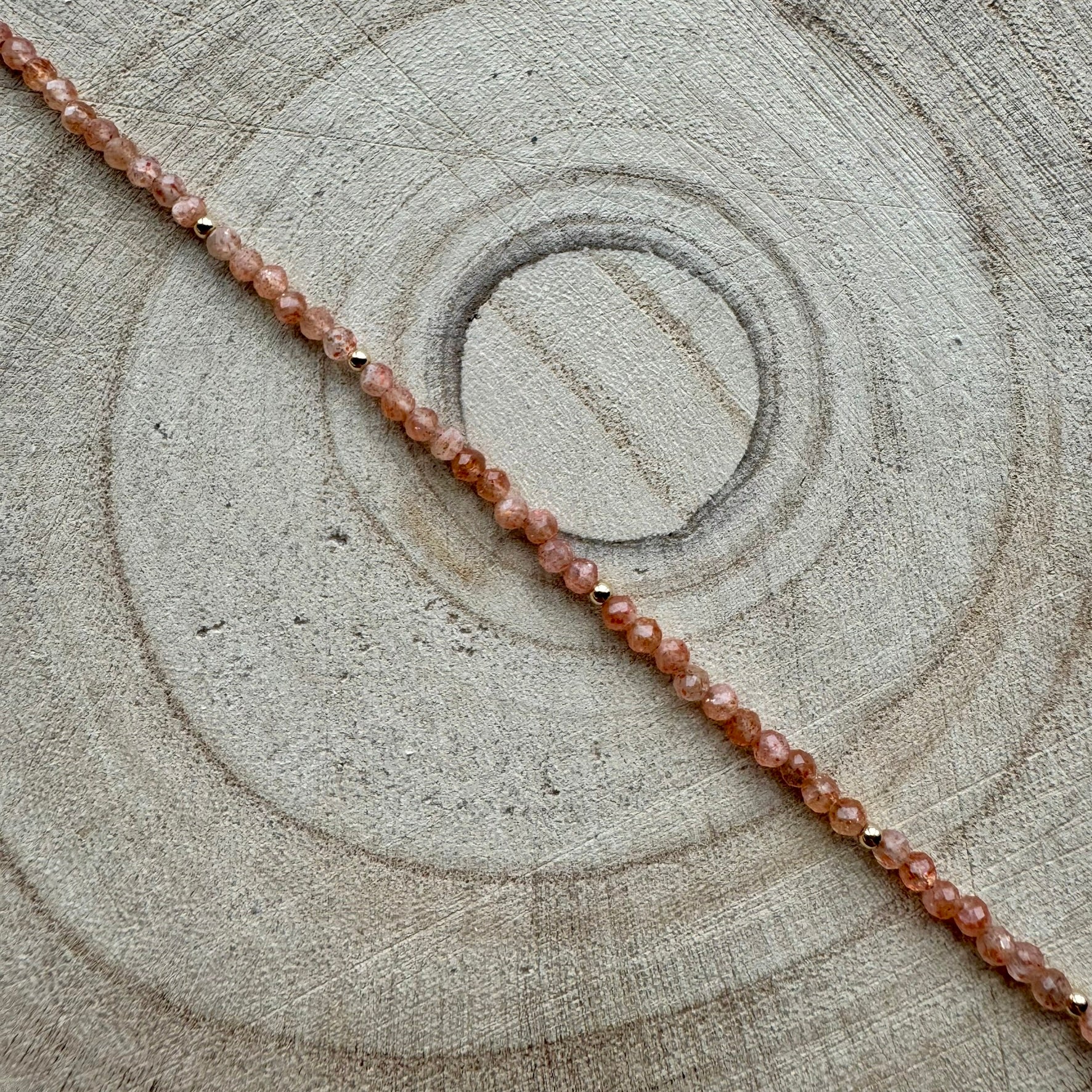 Peach sunstone bracelet with gold filled details on wooden surface