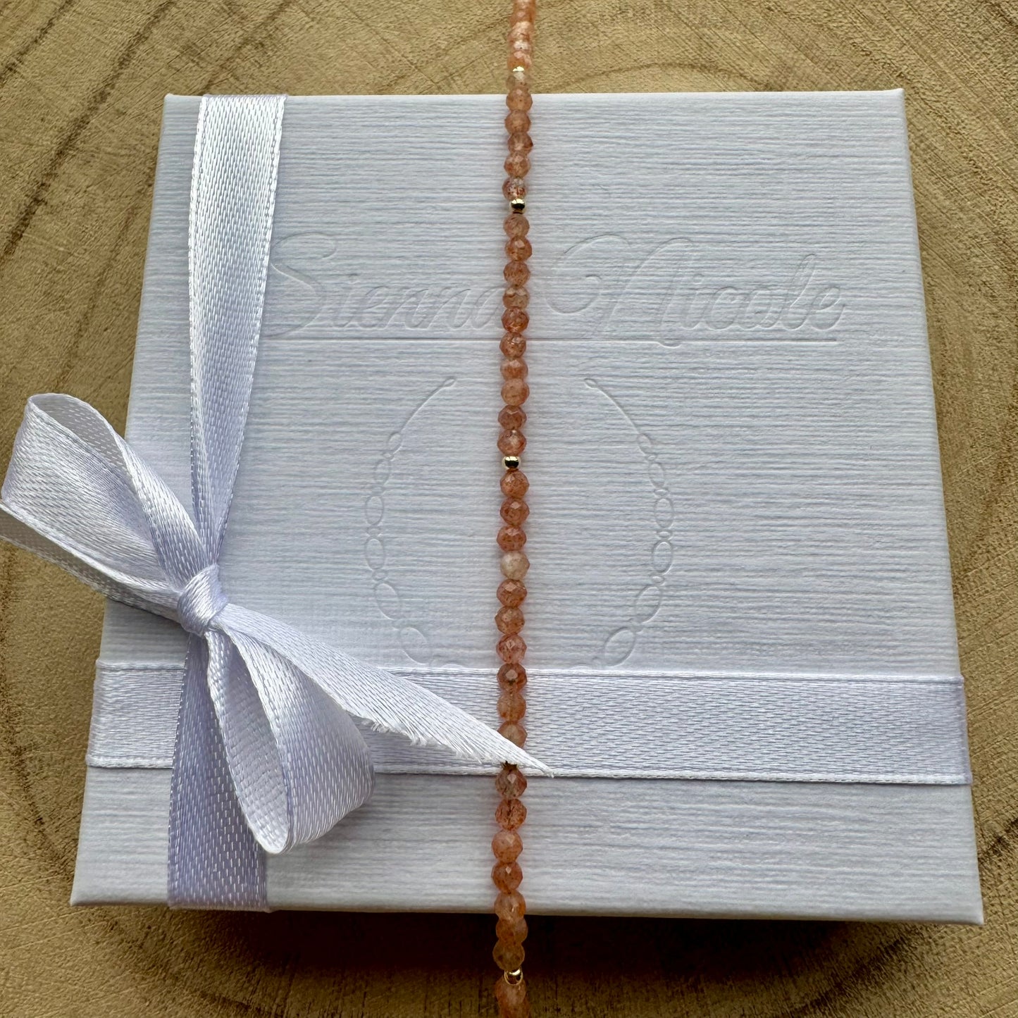 Vertical view of peach sunstone bracelet with gold filled details on white gift packaging