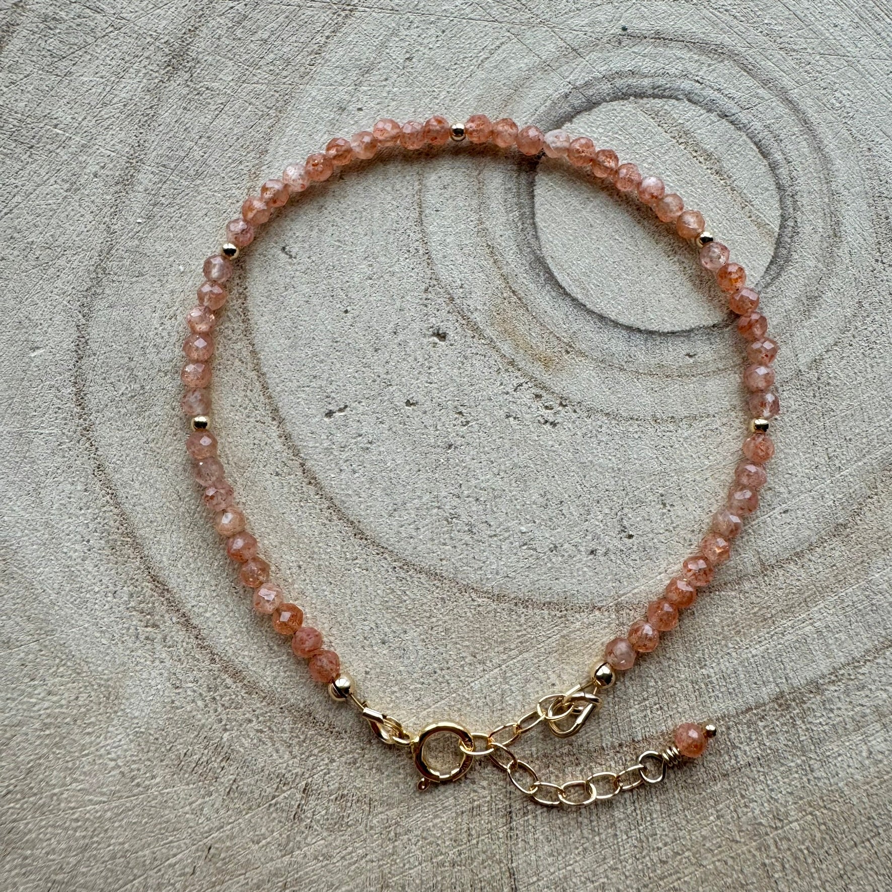 Peach sunstone bracelet with gold filled details on wooden surface